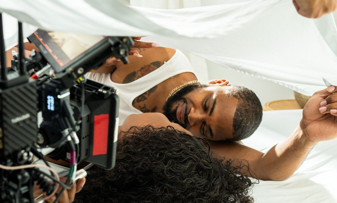 BTS photo of couple under sheets of bed with camera filming in Atlanta by LaTisha Guster photography